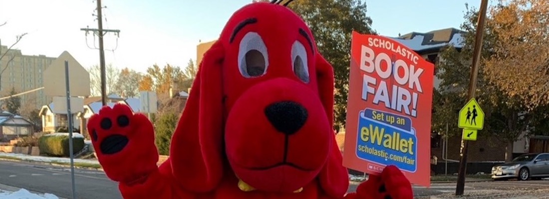 Clifford the Big Red Dog waving with a Book Fair sign