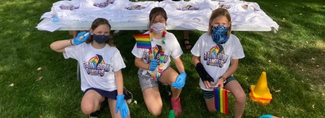 3 students posing on grass wearing masks and holding flags