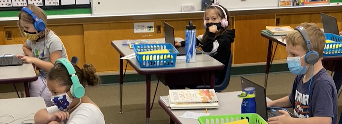 Students in class wearing masks and using laptop devices