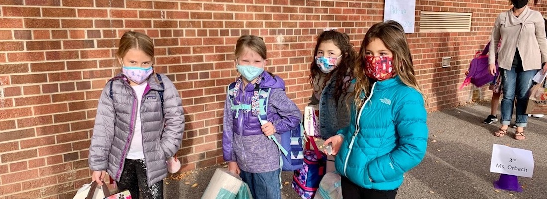 4 students posing with masks on outside of school