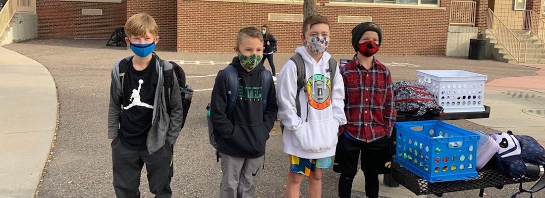 4 students wearing masks and standing outside of the school