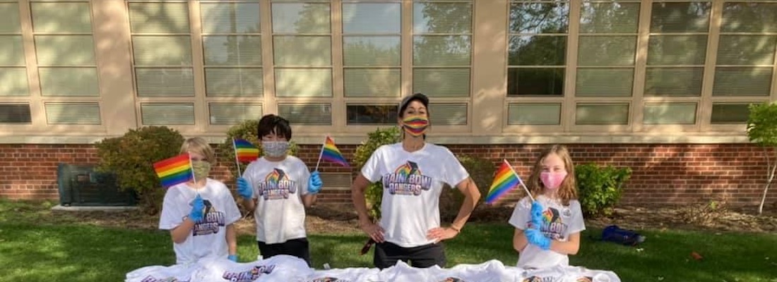 Students wearing masks in front of the school holding rainbow flags